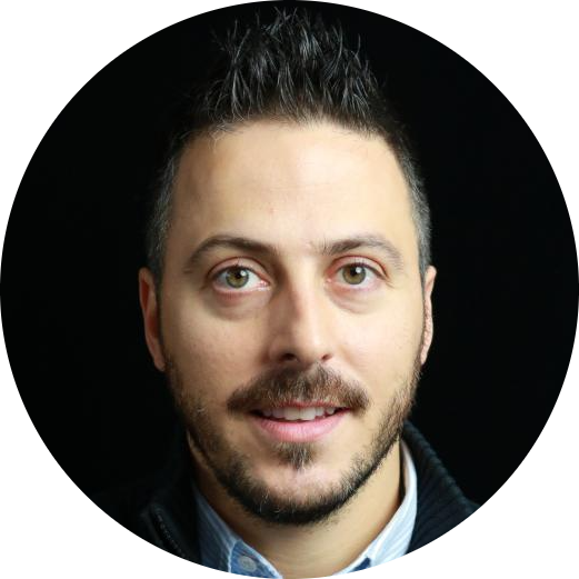 Professional headshot of an unidentified individual with short dark hair and a beard, standing against a dark background.
