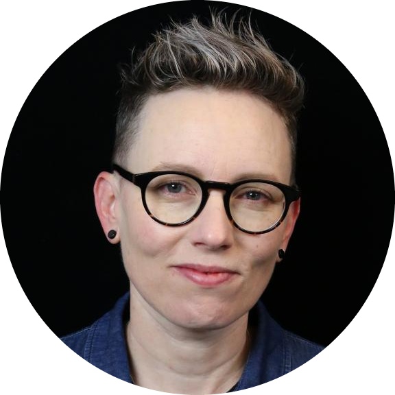 Headshot of individual with short hair, glasses, and earrings, on a black background