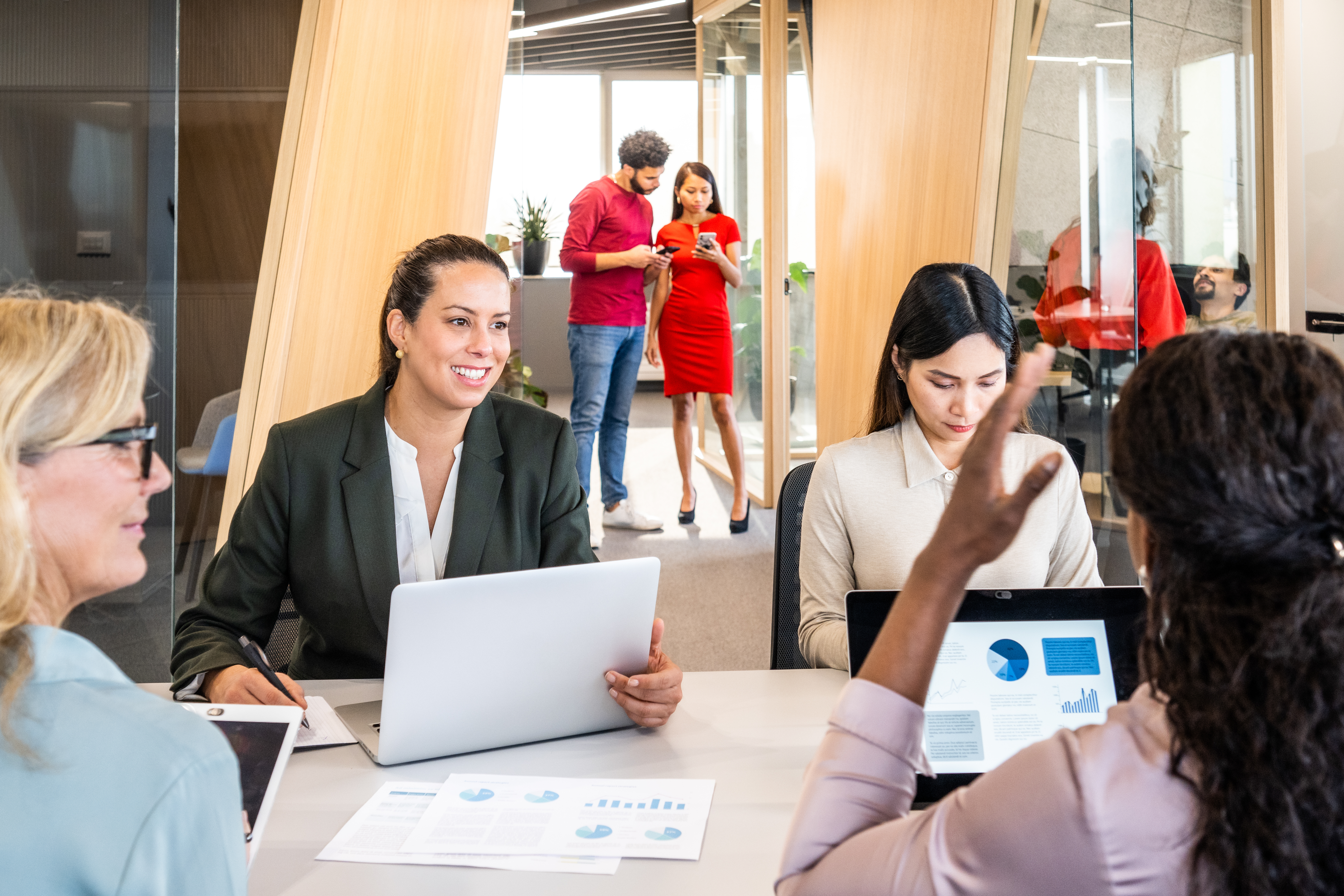Group of businesswomen at a meeting in an open plan office talking while using computers.