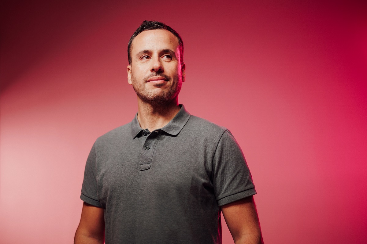 A person wearing a gray polo shirt against a pink gradient background.