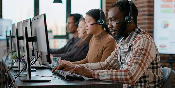 Customer service representatives wearing headsets working at desktop computers in a call center environment.