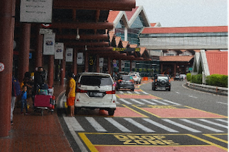 Vehicles and passengers in the designated drop-off zone at an airport terminal, illustrating traffic management and passenger flow.