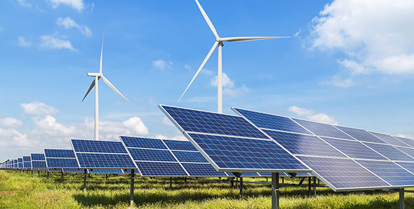 A renewable energy field with wind turbines and rows of solar panels under a blue sky with scattered clouds.