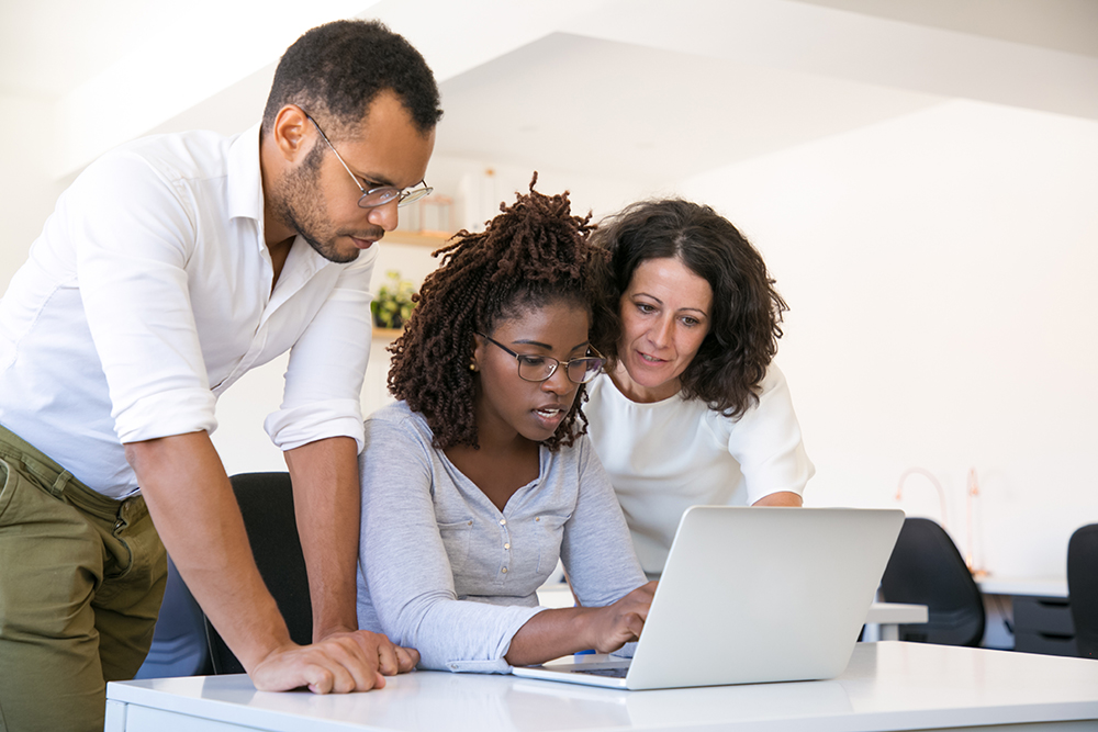Three colleagues collaborating and working together on a laptop in a modern office environment.