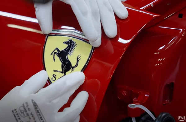 Close-up of gloved hands installing a Ferrari badge on the fender of a red sports car.