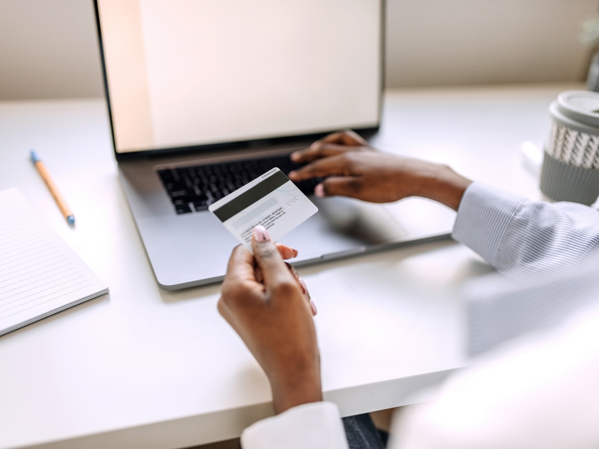 A person holds a payment card while making a purchase on a laptop