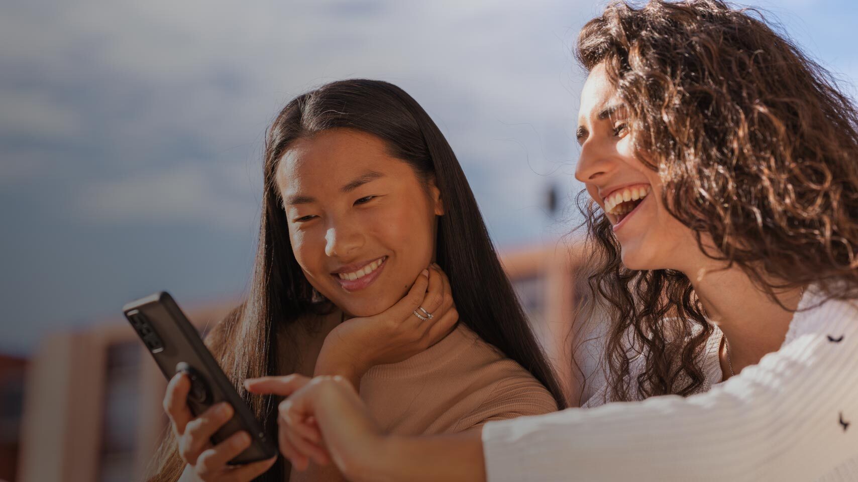 Two women looking at a smartphone and smiling outdoors