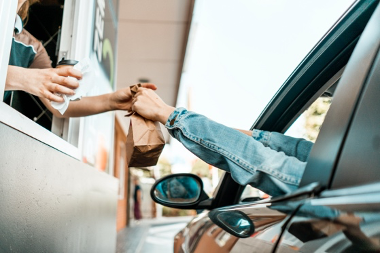 A person in a car receives a packaged food order from an employee at a drive-thru window, illustrating efficient drive-thru and curbside pickup service.