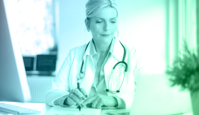 A female doctor with a stethoscope reviews information on a laptop in a bright office, representing cloud-based healthcare technology and machine learning applications in health.