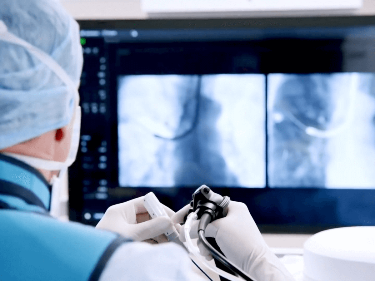 A doctor in medical attire is performing a medical imaging procedure, viewing radiology images on monitors in a healthcare setting.