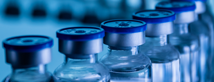 A close-up image of medicine bottles with blue caps aligned on a conveyor line, representing pharmaceutical manufacturing or healthcare processing.