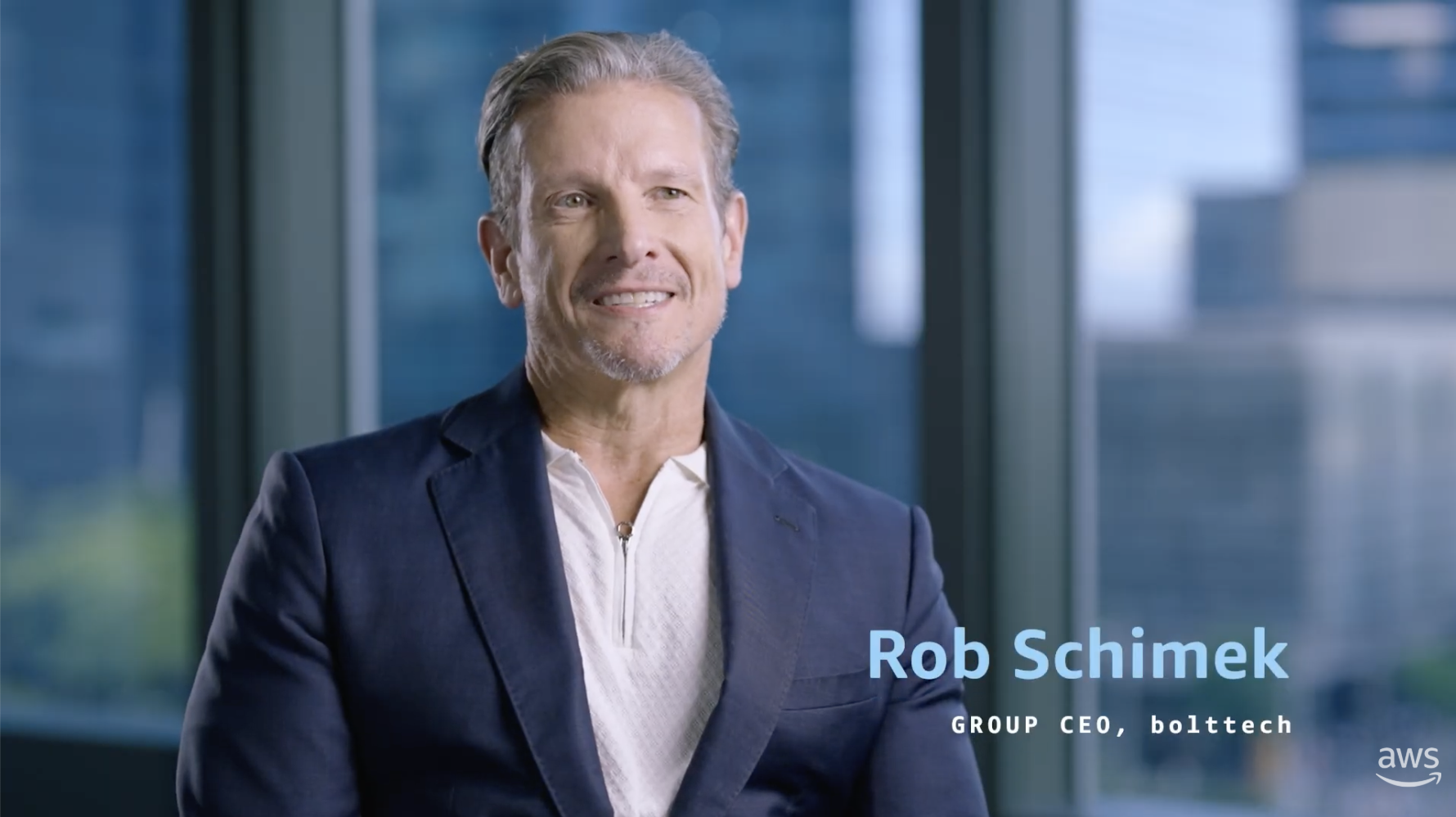 Text overlay reads "Rob Schimek, Group CEO, bolttech" with a blurred cityscape visible through large windows in the background.