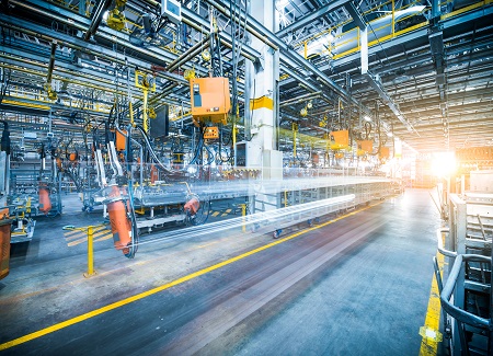 Modern factory interior with robotic arms and machinery, illuminated by bright sunlight.