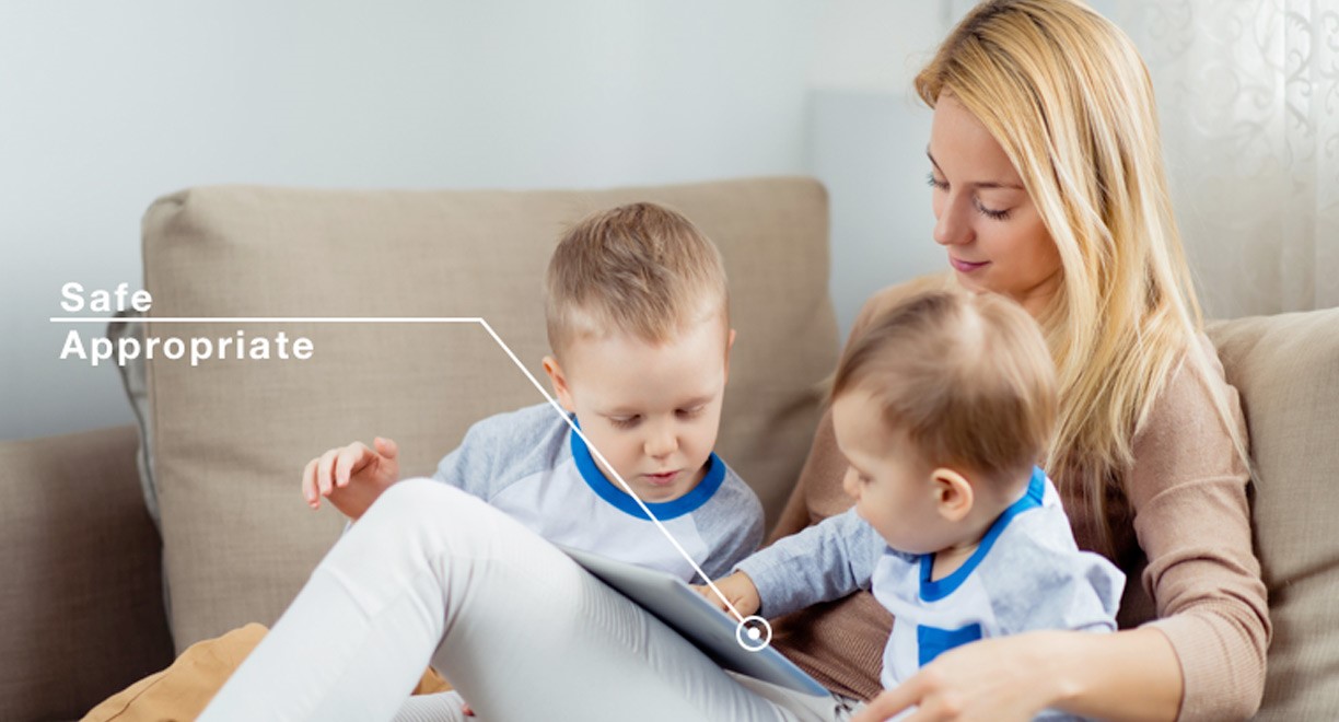 A mother sitting on a couch with two young children using a tablet, illustrating a safe and appropriate environment for children's device usage.