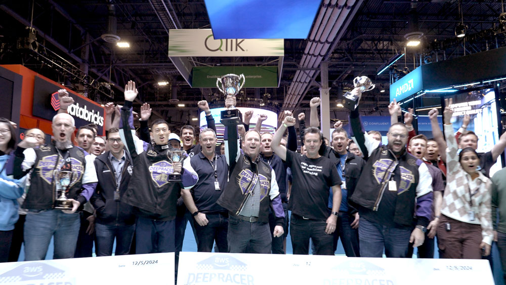 A group of people celebrating with raised fists and holding trophies at an event, surrounded by tech company banners.