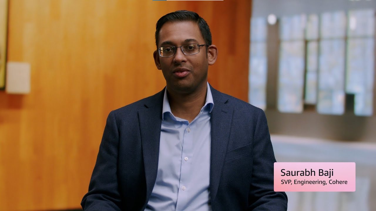 A person in a blue suit and light blue shirt sits in a room with wooden walls and large windows; a label reads "Saurabh Baji, SVP, Engineering, Cohere."