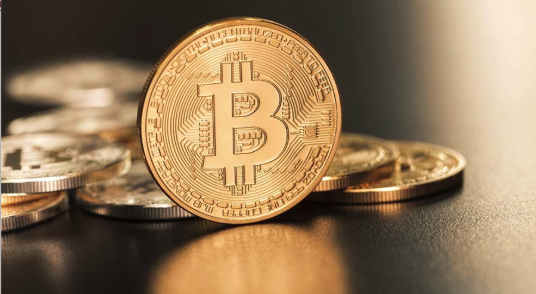 A close-up image of a physical coin representing the Bitcoin cryptocurrency, with several similar coins blurred in the background, symbolizing digital currency and blockchain technology.