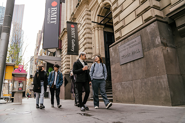 Students walking and chatting outside RMIT University's Storey Hall on a city street.