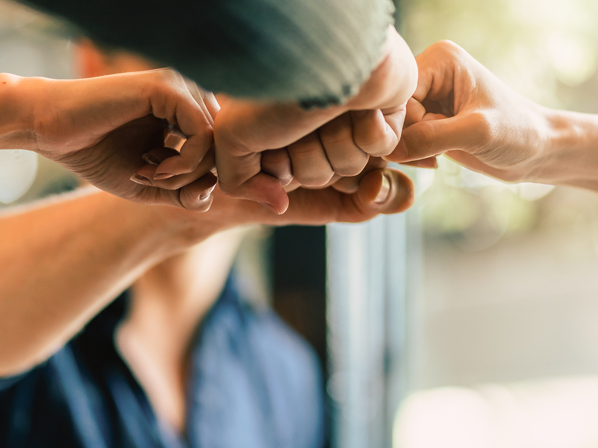 A close-up image of multiple hands coming together in a fist bump, symbolizing teamwork, collaboration, and unity during a creative agency business meeting.