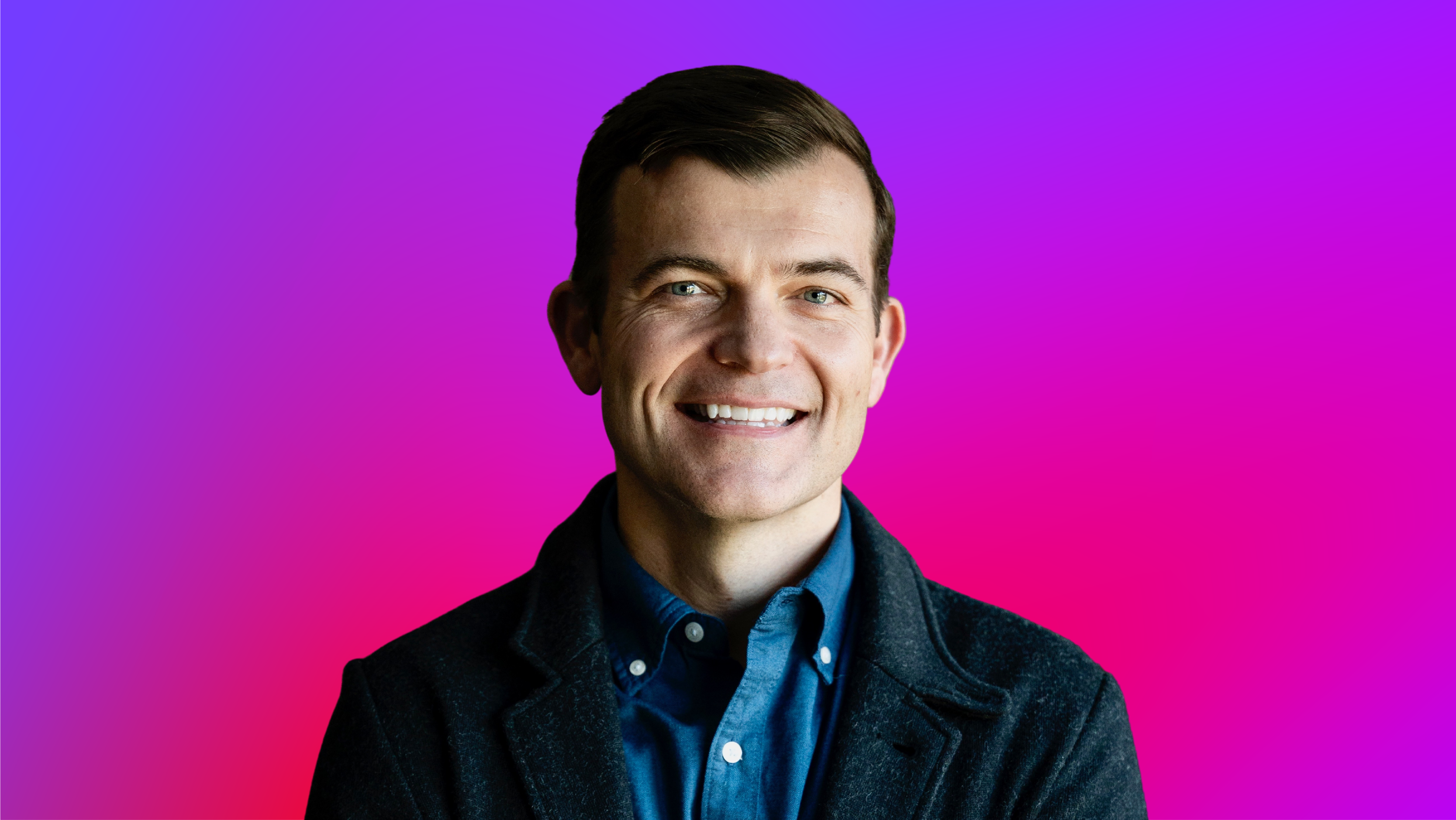 A person wearing a blue collared shirt and dark jacket against a vibrant purple-to-pink gradient background.