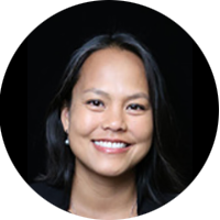 A professional headshot of a smiling woman with dark hair, wearing a dark top, against a black background. The image is presented in a circular crop.
