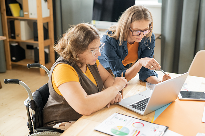 Two young serious female managers or brokers looking at laptop display while reading online data by workplace in office environment