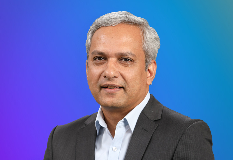 A professional headshot of a man in a business suit, set against a blue gradient background.