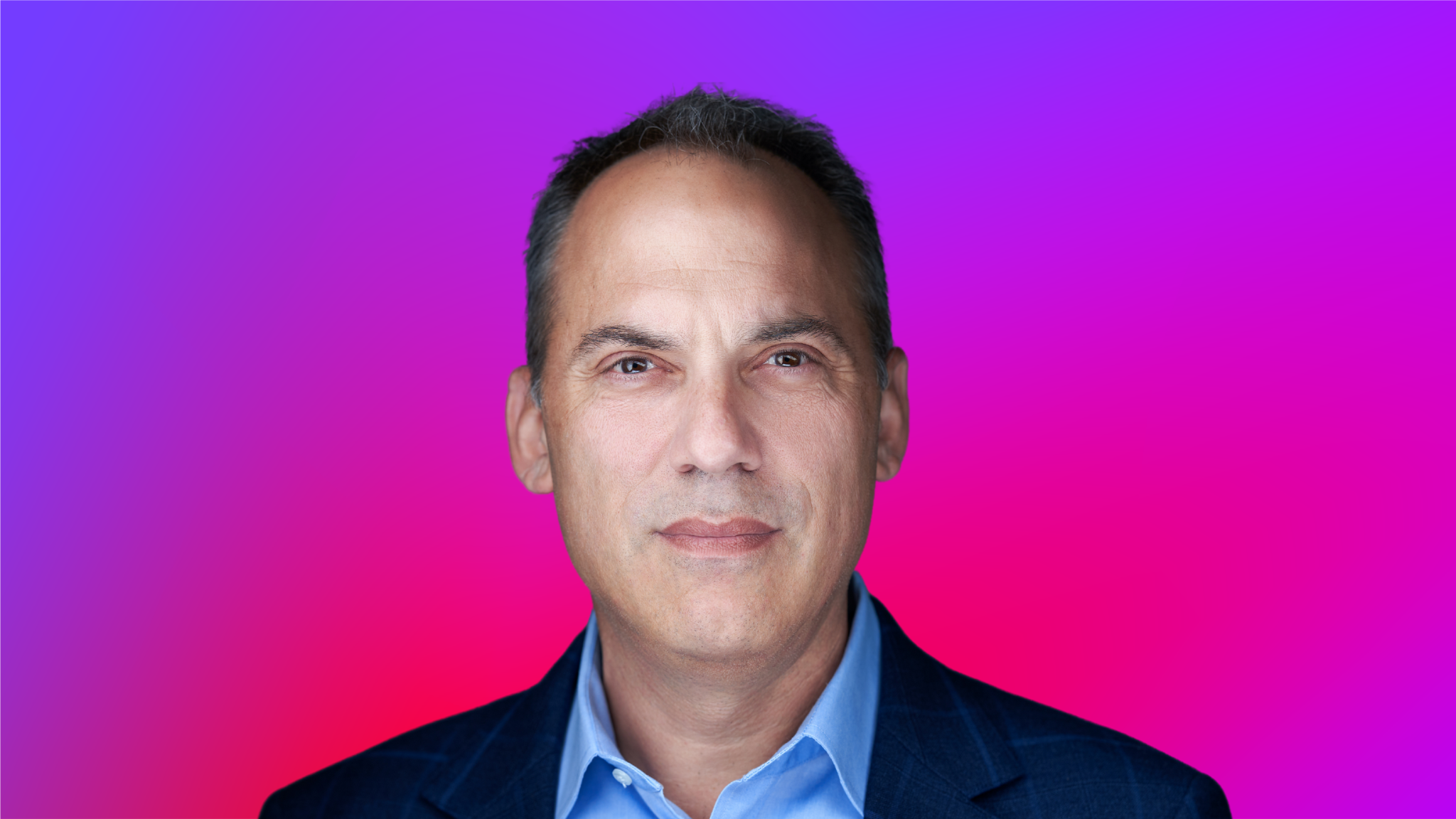 A person wearing a blue collared shirt and dark blazer against a vibrant purple and pink gradient background.
