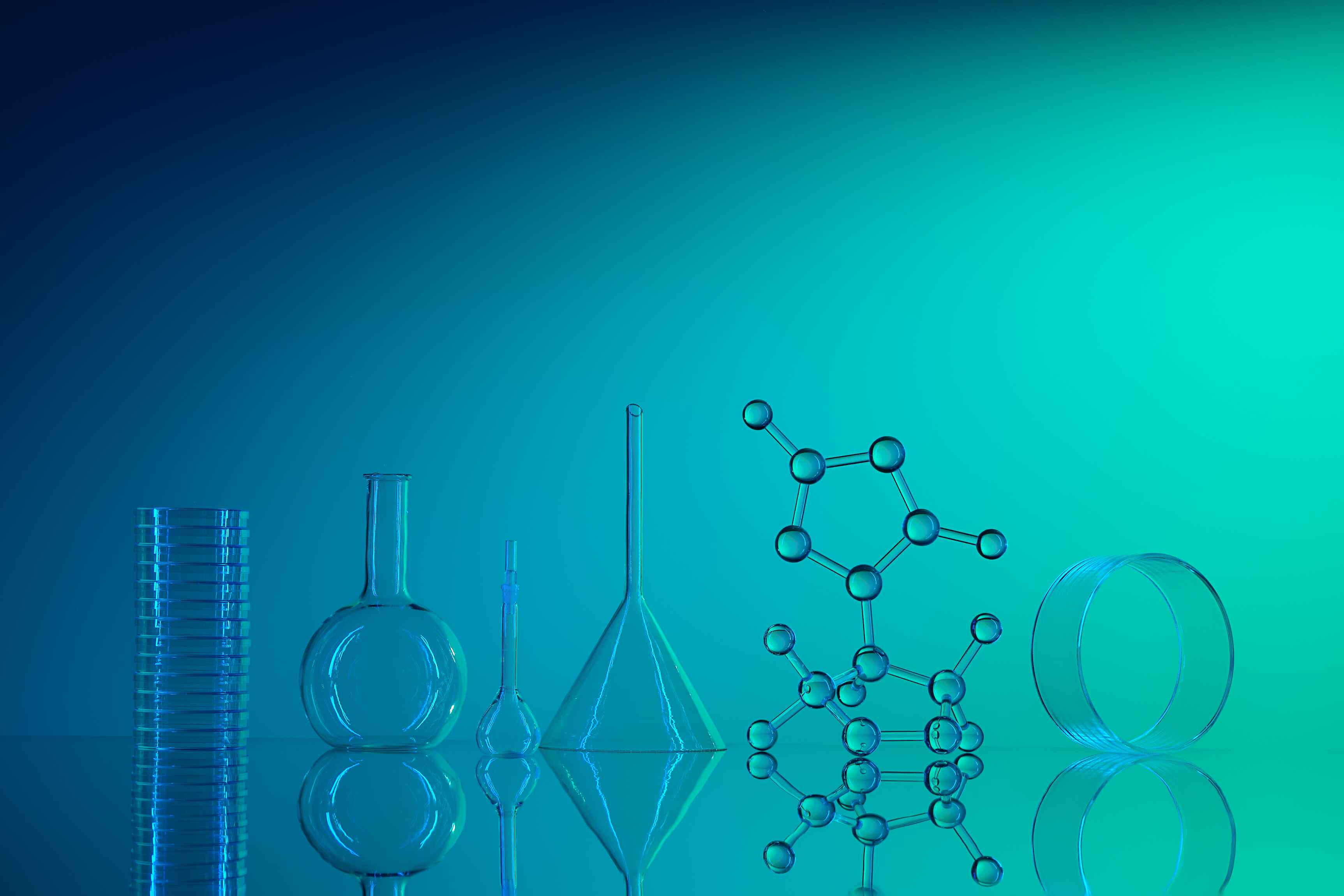 A collection of transparent laboratory glassware, including petri dishes, flasks, beakers, and a molecular structure model, arranged on a reflective surface against a blue gradient background.