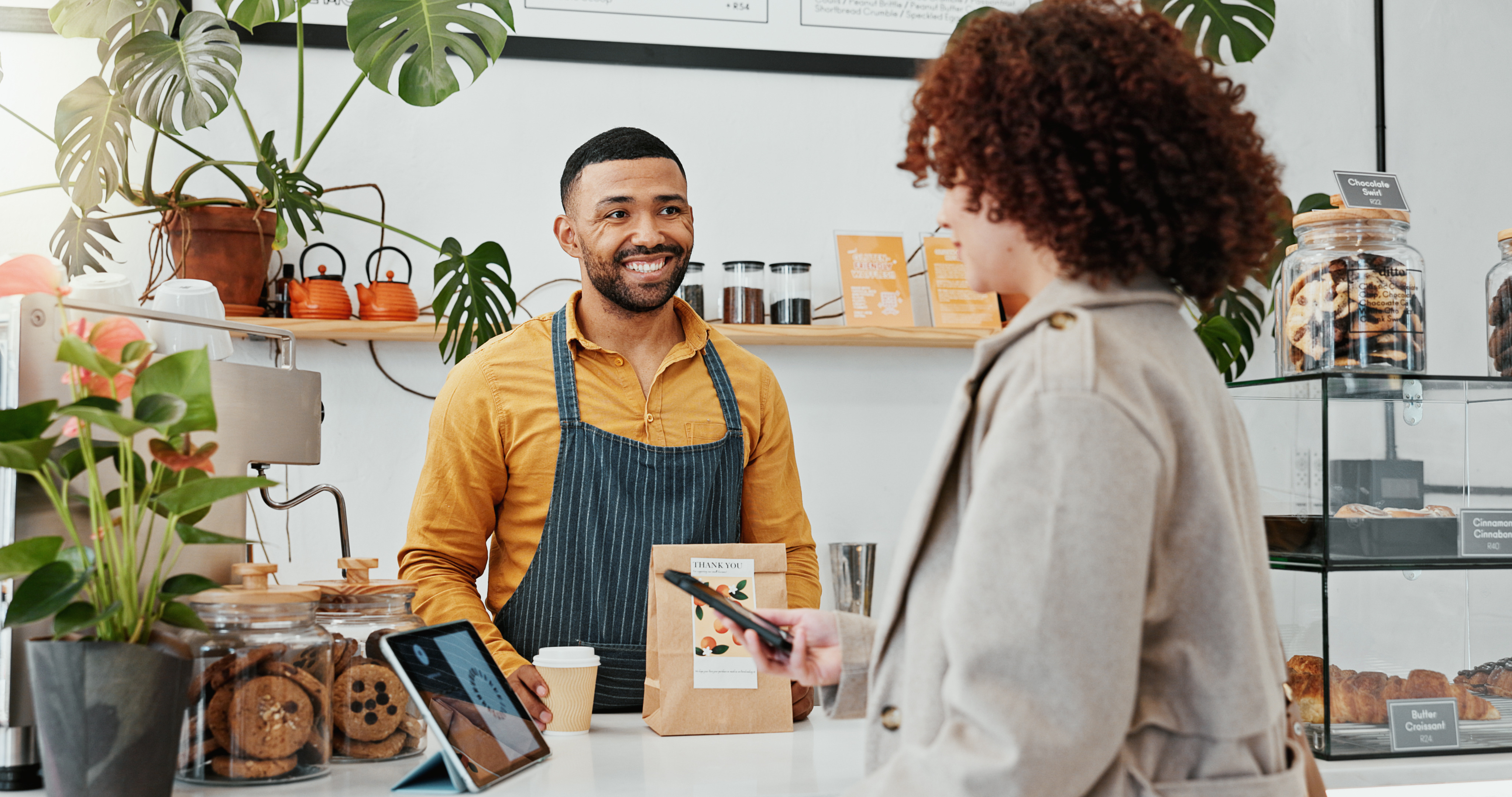 Woman, smartphone and tablet with cashier in coffee shop to pay for sale, ecommerce and digital checkout. Customer, happy and technology for internet banking, payment and online transaction in cafe
