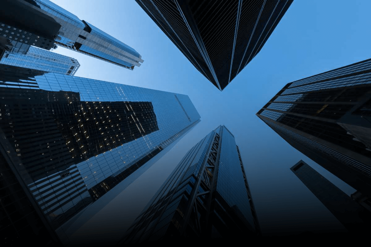 Upward view of modern skyscrapers against a blue gradient sky, featuring reflective glass buildings. Architectural image conveying scale and cloud financial management innovation.