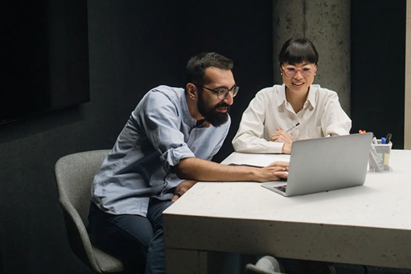 Two people collaborating on a laptop in an office setting