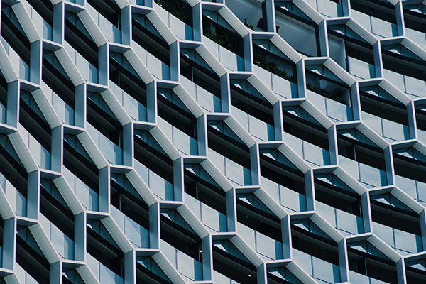 A modern building facade featuring a repeating geometric pattern made of angular, protruding structures and glass windows.