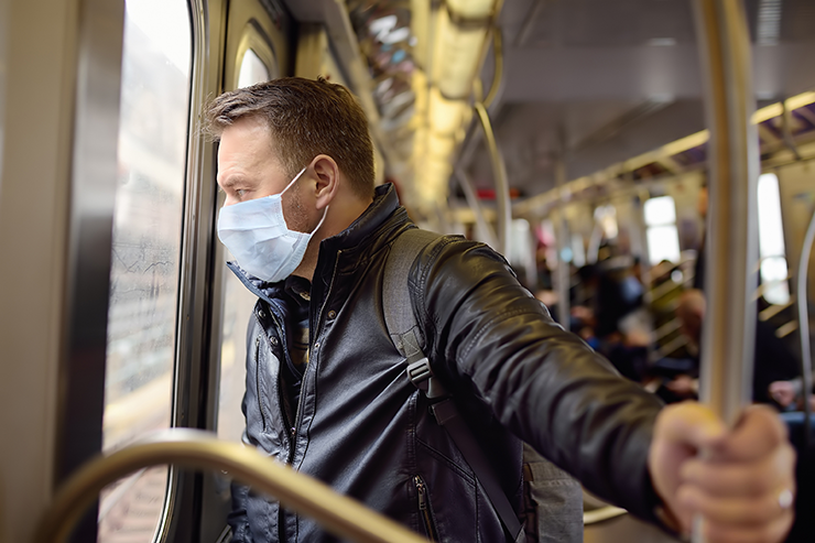 A person wearing a black leather jacket and backpack holds onto a subway pole while looking out the window.