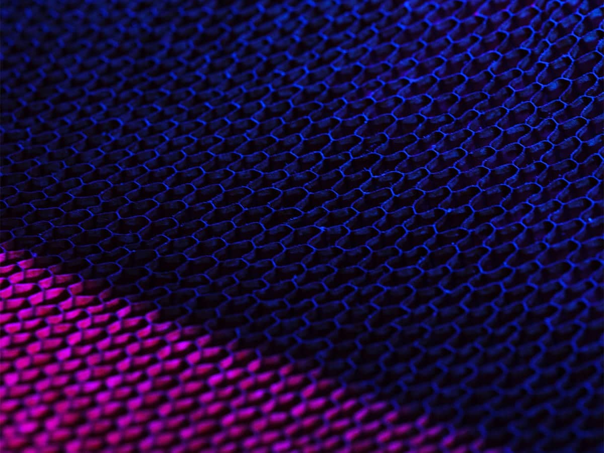 Close-up view of an abstract mesh texture with a repeating hexagonal pattern, illuminated in dark blue and purple lighting.