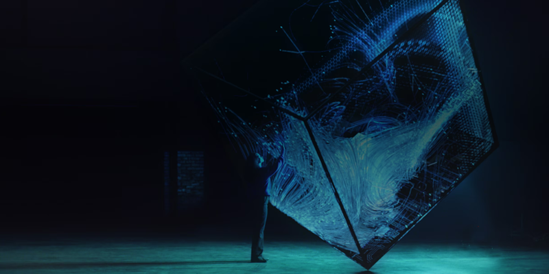 A person interacting with a large digital cube featuring illuminated blue data or circuitry patterns, representing ARM EDA workflows with AWS Batch in a technologically advanced and abstract environment.