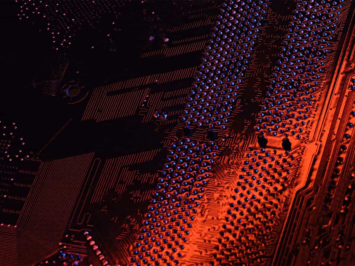 A closeup view of an electronic circuit board illuminated by red light, highlighting the intricate patterns and components.