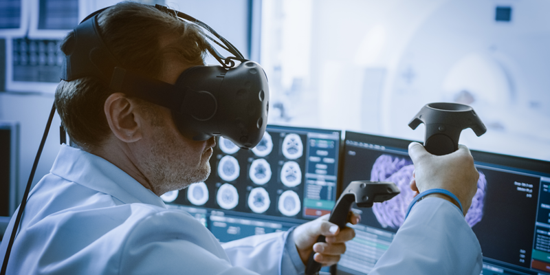 A person in a lab coat using virtual reality equipment to interact with brain scan images displayed on multiple monitors.