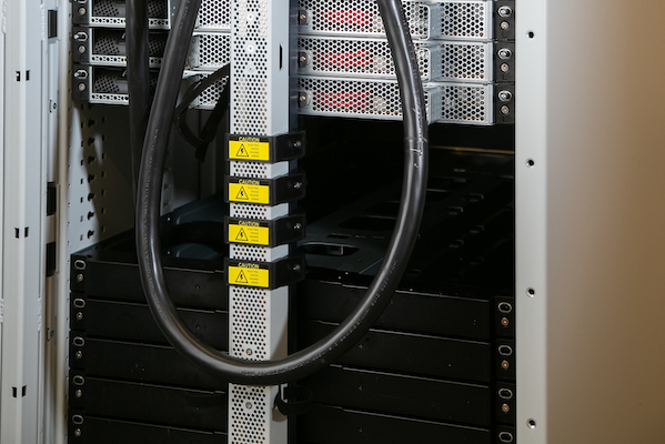 Close-up of a server rack with cables and components, featuring warning labels on several sections.