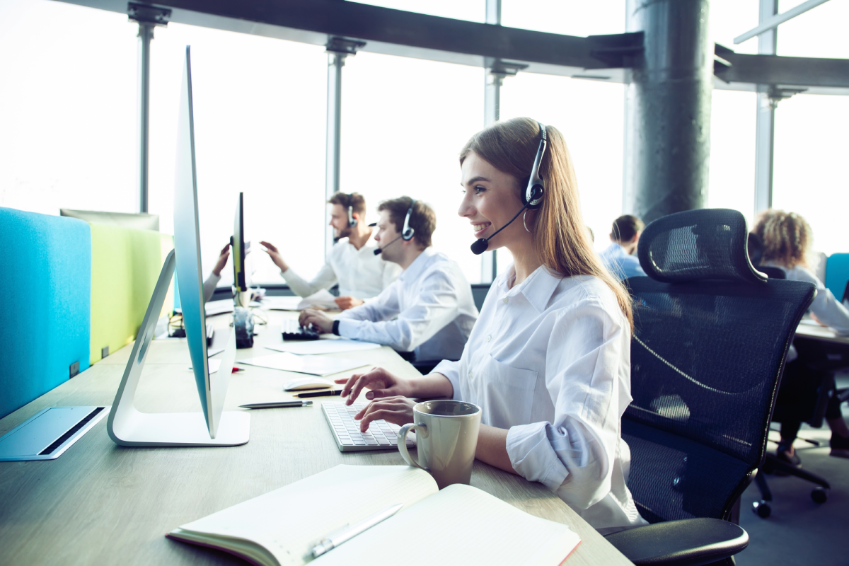 Customer service representatives wearing headsets working at computers in a modern contact center office environment.