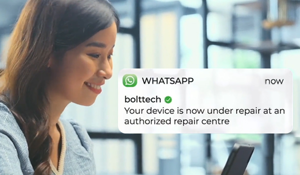 Alt-text: A WhatsApp notification from "bolttech" stating, "Your device is now under repair at an authorized repair centre," displayed over a blurred background of a modern office setting.
