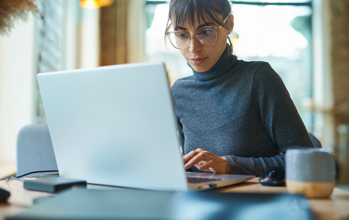 Person wearing a gray sweater working on a laptop at a desk in a bright, modern setting.