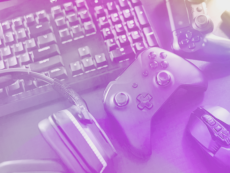 Gaming setup with a keyboard, headphones, controllers, and a mouse, tinted in purple light.