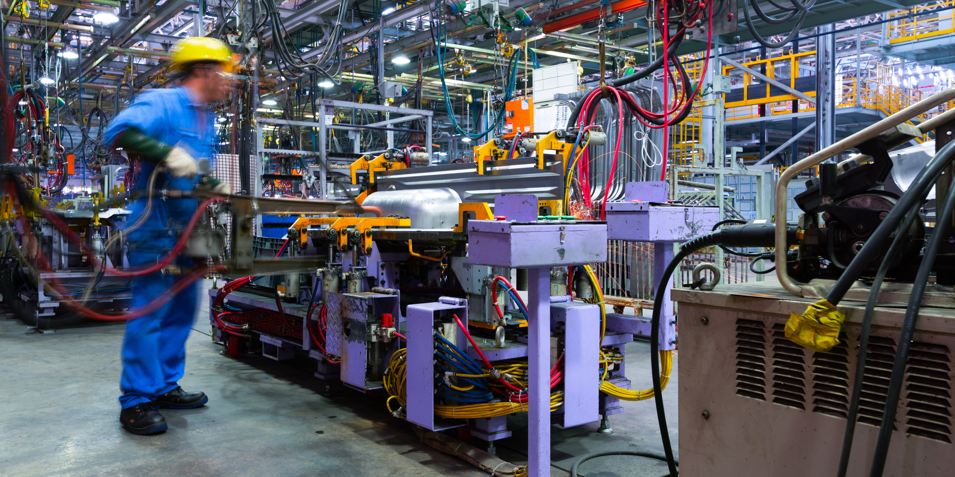 A busy factory floor with industrial machinery, colorful cables, and metal components under bright lighting.