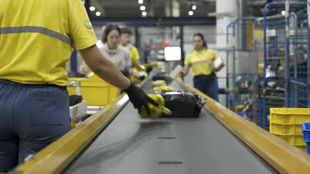 Workers in yellow uniforms sorting packages on a conveyor belt in a warehouse setting.