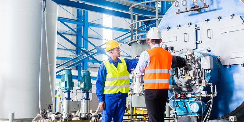 Two workers in safety gear inspecting industrial machinery in a factory setting.