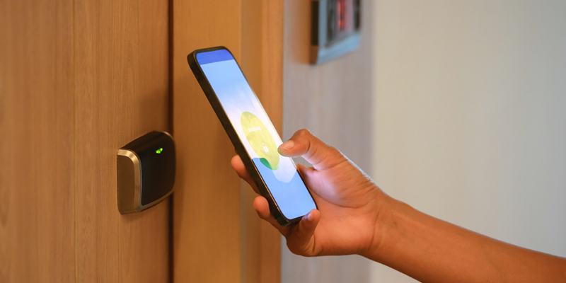A person holding a smartphone near a digital door lock, unlocking it with a mobile app.