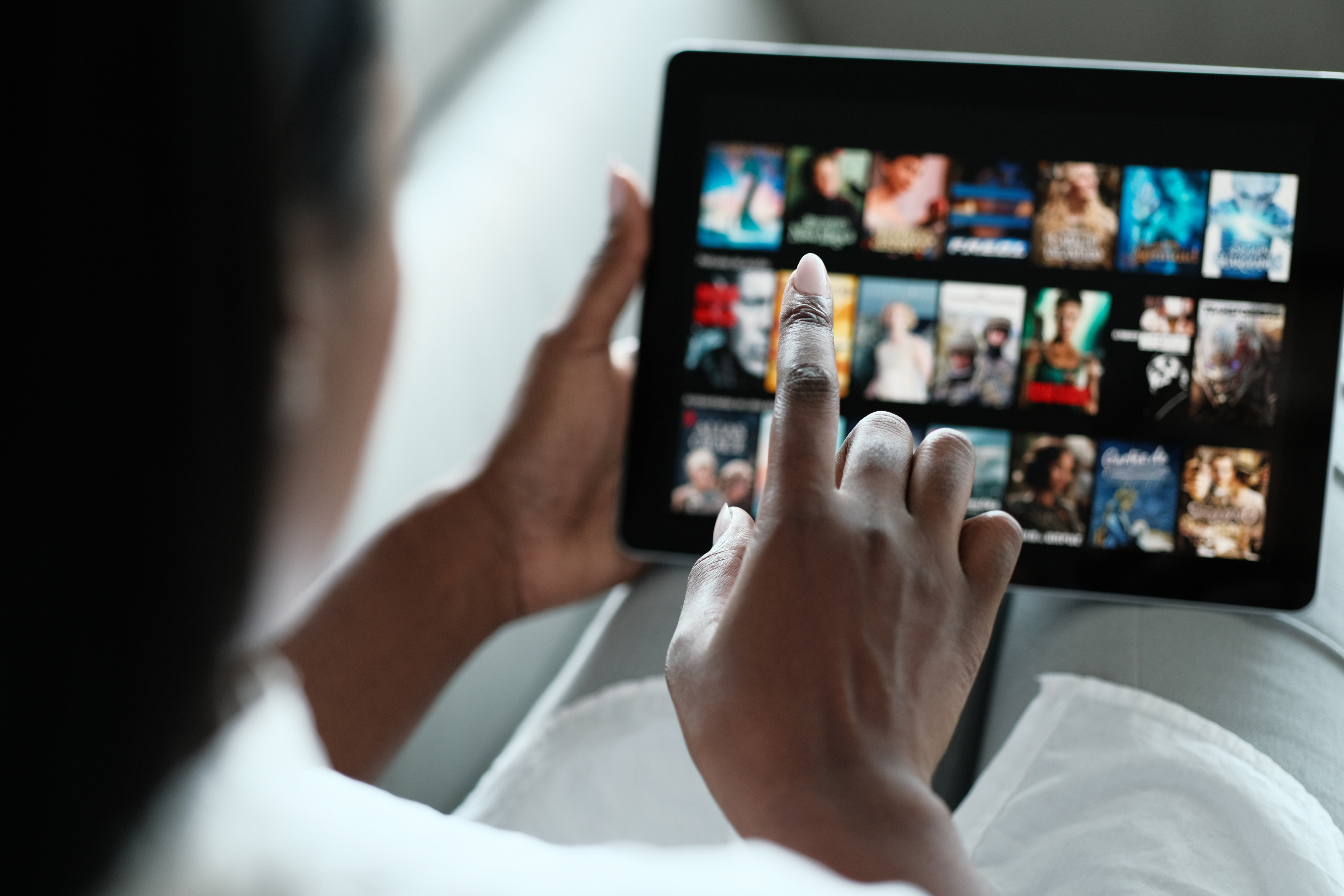 A person using their finger to browse a selection of movies or TV shows on a streaming media app on a tablet device.