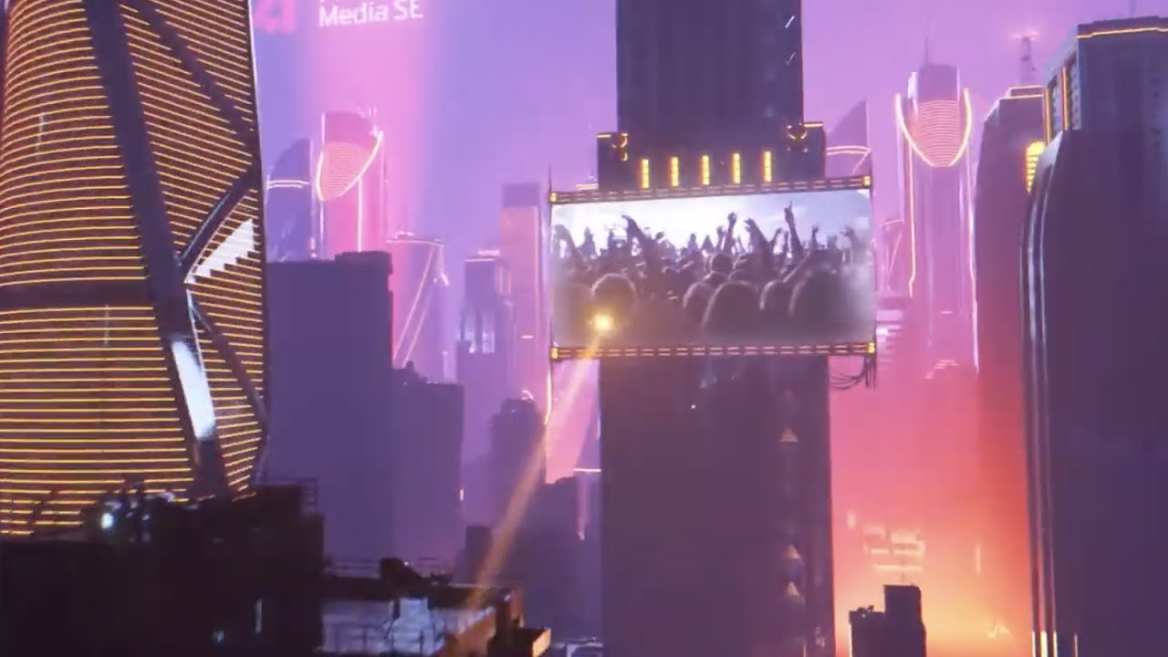 A vibrant futuristic cityscape at sunset featuring high-rise buildings illuminated with neon lights. A large digital billboard on one skyscraper displays a cheering crowd, suggesting a concert or event in a lively urban environment.