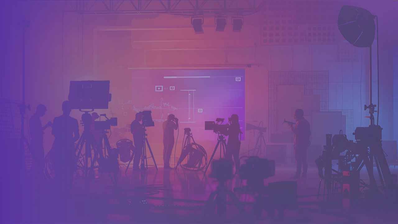 Silhouettes of people and cameras in a studio with a large screen displaying graphs and data in the background, illuminated by purple and pink lighting.